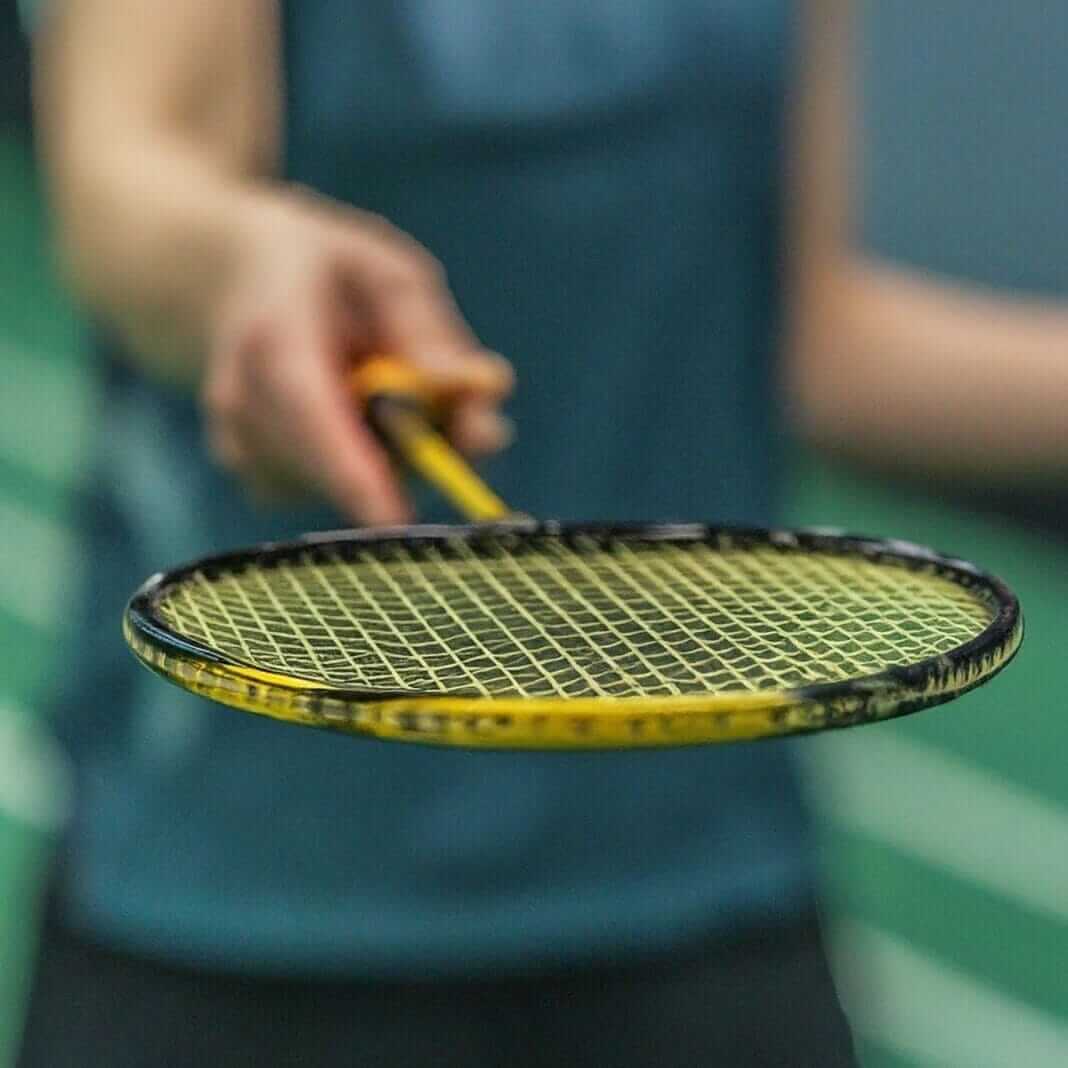 A person holding a badminton racket on a court, ready to play a game of badminton.