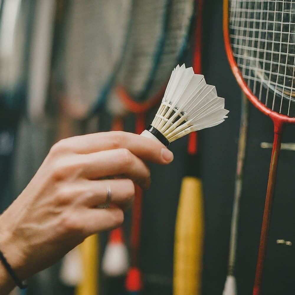 A person holding a badminton racket and shuttlecock, selecting a racket in a sports shop